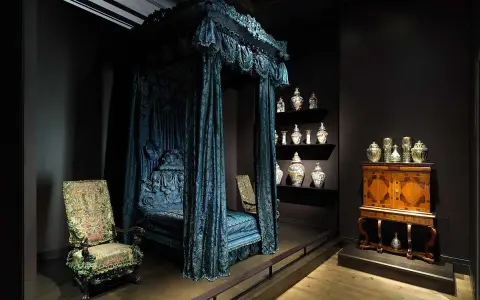 Cama con dosel azul, sillas ornamentadas y vitrinas con cerámica, como si fueran escenarios de cursos de arte online.