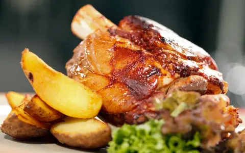 Codillo de cerdo asado, crujiente y jugoso, acompañado de patatas gajo doradas y una guarnición verde.