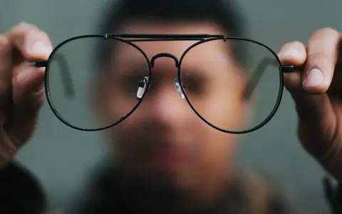 Osoba trzyma okulary przed twarzą. Chcesz wiedzieć, co zrobić, żeby nosić okulary?