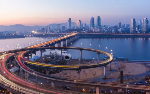 Verkehrsfluss in Seoul bei Nacht, mit Lichtern, die sich auf den Autobahnauffahrten und der Skyline der Stadt spiegeln.