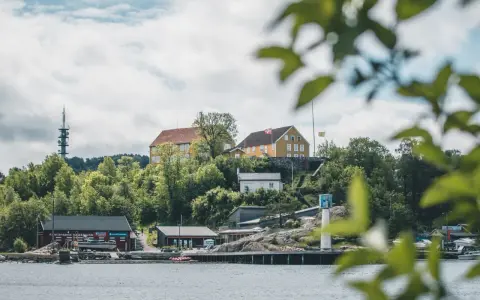 Widok na wybrzeże w Kristiansand, Norwegia. Żółte budynki na wzgórzu, czerwony klub kajakowy i wieża telekomunikacyjna.