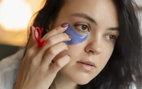 Una mujer se aplica parches de ojos morados. Muestra cómo se ponen los parches de ojos para un cuidado facial.