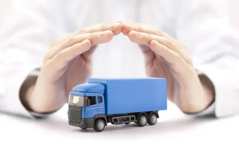 Ręce chronią niebieską ciężarówkę, symbolizując ubezpieczenie AC w kosztach transportu.