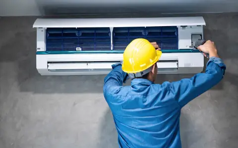 Técnico con casco amarillo revisa la unidad interior de aire acondicionado, buscando la causa del ruido.