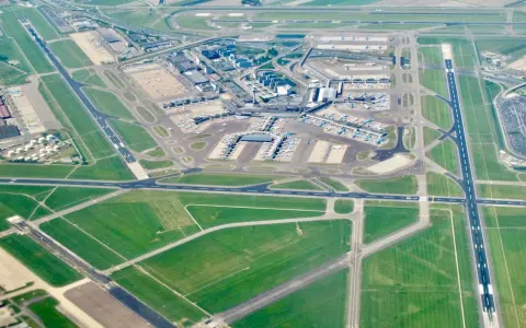 Ögonblicksbild över ams flygplats med flygplan på marken och i luften, omgivet av gröna fält och vägar.