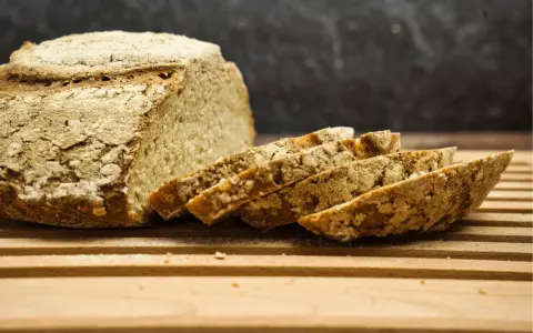 Ein rustikales, selbstgebackenes Brot liegt angeschnitten auf einem Holzbrett. Die Kruste ist knusprig, die Scheiben duften nach Tradition.