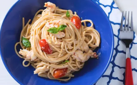 Un plat de pâtes aux crevettes, tomates cerises et basilic, servi dans un bol bleu vif. Un délice !