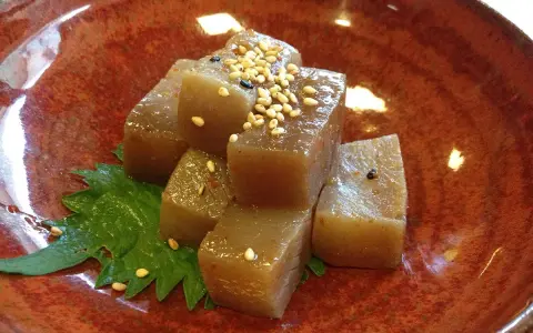 A simple dish of konjac jelly cubes, seasoned with sesame seeds and chili flakes, served on a green leaf in a rustic bowl. This is what monks eat.