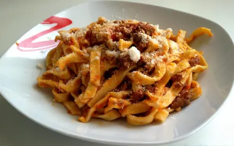 Un piatto invitante di tagliatelle al ragù, condite con abbondante parmigiano grattugiato.