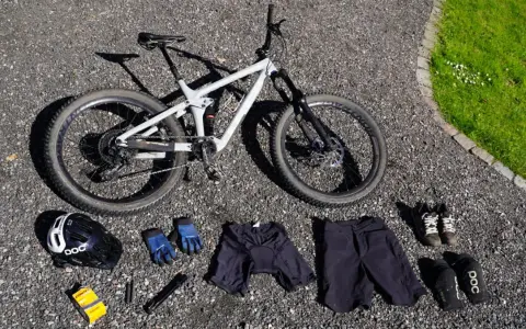 Fullt utrustad för en dag på stigarna: en grå heldämpad cykel, hjälm, handskar, shorts, skor och skydd. Allt för din mtb utrustning.