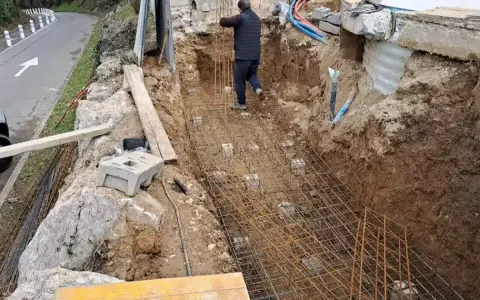 Un ouvrier travaille sur le ferraillage d'une fondation. Des armatures métalliques sont posées dans une fouille creusée dans la terre.