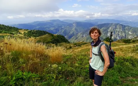 Donna con zaino e bastoncini da trekking ammira il panorama montuoso, un'emozione delle camminate FVG.