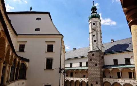 Dziedziniec zamku w Bruntalu, Czechy. Białe mury, arkadowe krużganki i wysoka wieża zegarowa pod błękitnym niebem.