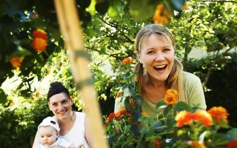 Två glada kvinnor och en bebis i en trädgård, kanske på en tipspromenad med 12 frågor bland blommorna.