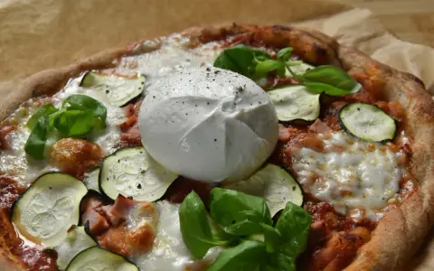 Pyszna pizza z burrata, cukinią i bazylią, posypana świeżo mielonym pieprzem.