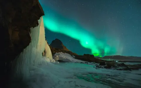 Lodowy wodospad i zorza polarna na nocnym niebie. Islandia w styczniu, magiczny widok.