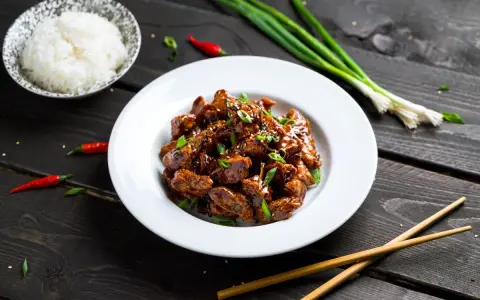 Pyszny kurczak po sajgońsku w sosie, posypany szczypiorkiem i sezamem, obok miseczka ryżu, pałeczki i papryczki chili.