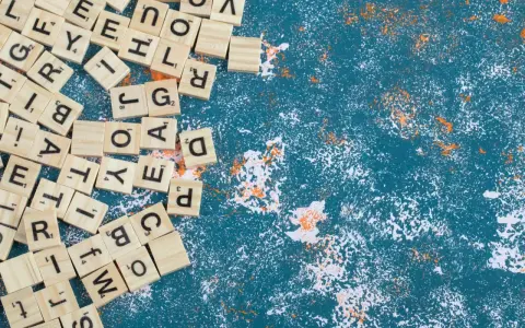 Fichas de letras de madera esparcidas, algunas formando palabras con w, sobre un fondo azul texturizado con salpicaduras blancas y naranjas.