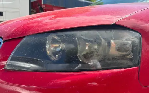 Faros sucios de coche rojo. El faro izquierdo muestra un anillo de luz, el derecho está rayado. La luz marcha atrás obligatoria es esencial para la seguridad.