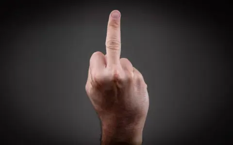 Eine Hand zeigt den Mittelfinger. Dies kann als Geste der Ablehnung oder als Zeichen der Rebellion gesehen werden, die eine Strafe nach sich ziehen kann.