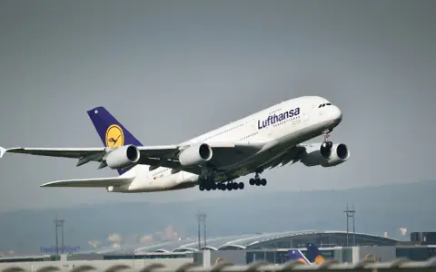 Samolot pasażerski Lufthansa z wysuniętym podwoziem startuje na tle lotniska.