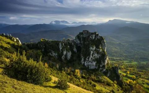 Ruines d'un château cathare sur un pic rocheux, dominant un paysage de montagnes et de forêts. Le chemin des bonshommes serpente à travers la vallée.