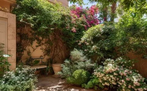 Un rincón acogedor con abundantes plantas enredaderas, flores rosas y blancas, y un banco bajo la sombra.