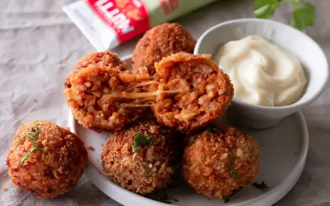 Was sind Arancini? Knusprig frittierte Reisbällchen mit geschmolzenem Käse, serviert mit einer cremigen Dip-Sauce.