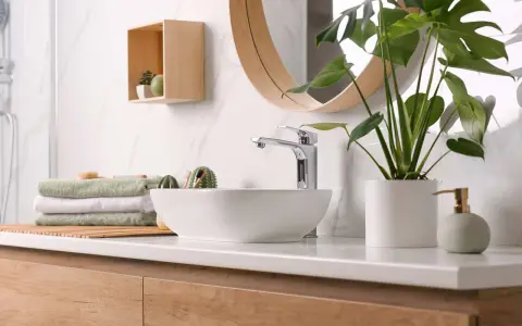 Plan de travail de salle de bain moderne avec vasque, robinetterie chromée, serviettes pliées et plante verte. La hauteur du plan de travail est idéale.