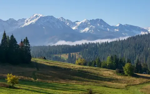 Widok na Tatry z Gubałówki. W oddali ośnieżone szczyty, niżej las i zielone zbocza. Widać fragment kolejki.