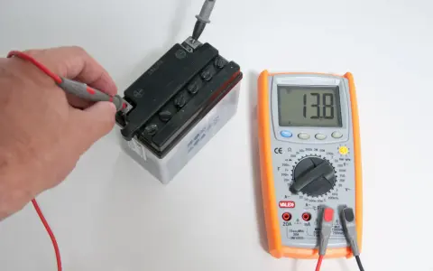 Una mano usa il multimetro per misurare la tensione di una batteria, mostrando 13.8V.