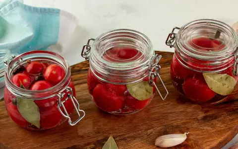 Słoiki z pysznymi, domowymi kiszonymi pomidorami, doprawione liściem laurowym i pieprzem. Idealne na zimę!