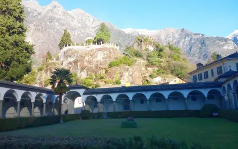 Un porticato ad archi domina un giardino curato, con montagne imponenti sullo sfondo. Un luogo ideale per scoprire cosa vedere a Chiavenna.