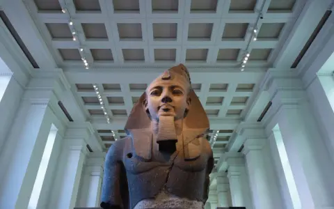 A colossal bust of an ancient Egyptian pharaoh, one of the museum's famous sculptures, stands majestically under a grand, coffered ceiling.