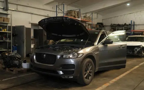 Grauer Jaguar XE mit geöffneter Motorhaube und Tür in einer Werkstatt, bereit für Reparaturen wegen Jaguar XE Probleme.