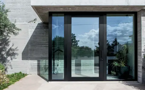 Puerta de entrada moderna con grandes ventanales de cristal, mostrando diferentes tipos de cristales para puertas exteriores que reflejan el cielo y la vegetación.