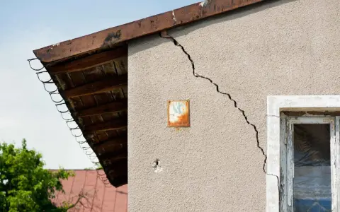 Grieta en pared de edificio, indicando problemas de **seguridad estructural**. Se observa un alero de madera y un cielo azul.