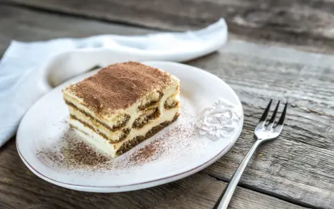 Une part de tiramisu maison, saupoudrée de cacao, sur une assiette blanche, prête à être dégustée. La conservation de ce délice est essentielle pour en savourer chaque bouchée.