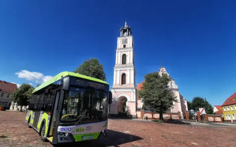 Zielony autobus MZK Chodzież czeka na pasażerów pod wieżą kościoła. Sprawdź mzk chodzież rozkład jazdy i zaplanuj podróż!