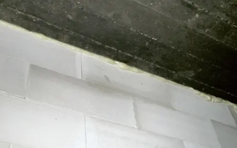 Piana montażowa wypełnia szczelinę między betonowym stropem a białą ścianą z bloczków, tworząc dylatację.