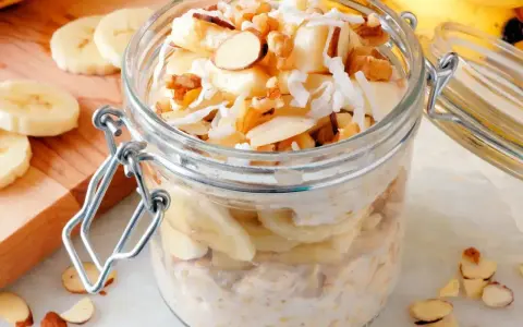 Słoik pełen pysznej owsianki z bananem, posypanej wiórkami kokosowymi i orzechami. Idealne śniadanie!