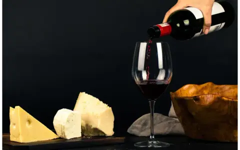 Vin rouge versé dans un verre, à côté de morceaux de fromage. La question "quoi boire avec une raclette" trouve ici une réponse évidente.