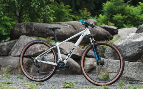 Biały rower Cube z brązowymi oponami, idealny jako rower na długie trasy. Wyposażony w amortyzator RockShox i napęd Shimano.