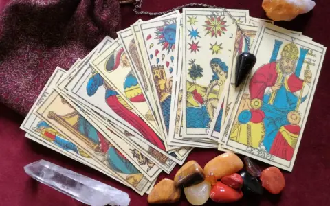 Cartas de tarot psicológico, un péndulo y cristales dispuestos sobre una tela burdeos.