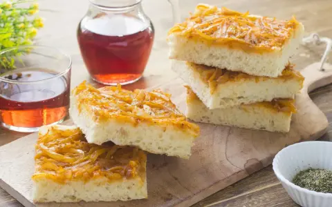 Focaccia con cipolle dorate e soffice, servita su un tagliere di legno con un bicchiere di vino rosato.