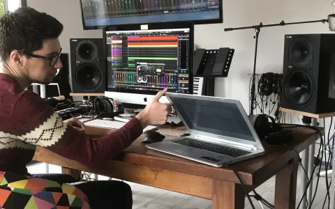Un jeune sound engineer travaille dans son studio, entouré de matériel audio, d'écrans et d'un clavier.