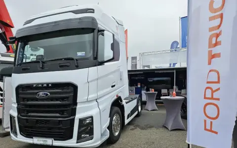 Biały Ford F-MAX prezentuje się na wystawie, obok banerów z logo Ford Trucks.