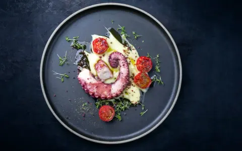 Un tentacolo di polpo alla griglia, servito su purè di patate con pomodorini confit e timo.