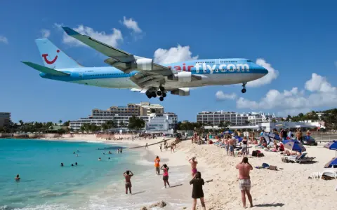 Samolot Airfly.com przelatuje nisko nad plażą pełną turystów, którzy obserwują jego lądowanie.