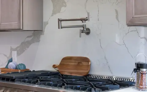 Składany kran nad kuchenką gazową, deska do krojenia i przyprawniki na blacie.